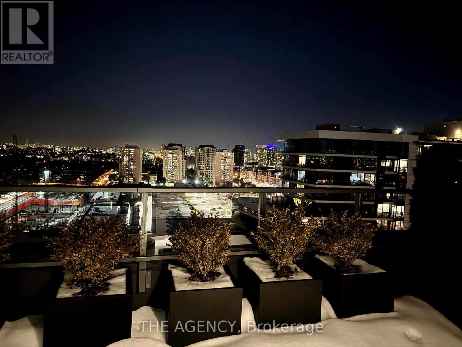 A nighttime cityscape with a view of the skyline and a building with the sign "THE AGENCY B. Brokerage".