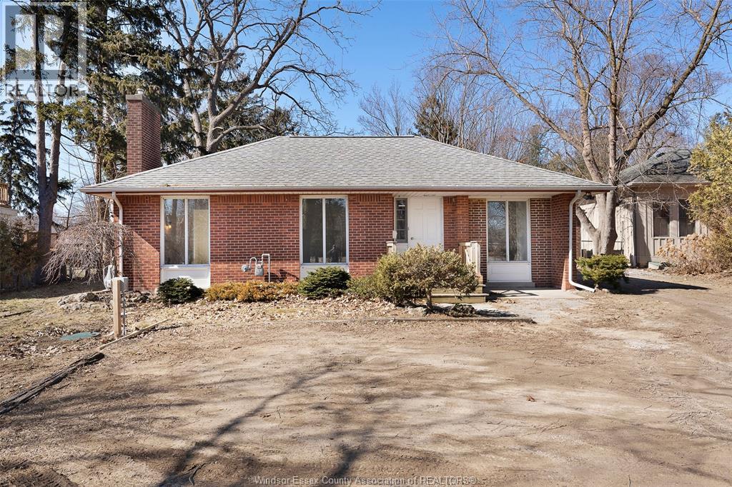 A house with a brick exterior and a grey roof is surrounded by a gravel driveway.