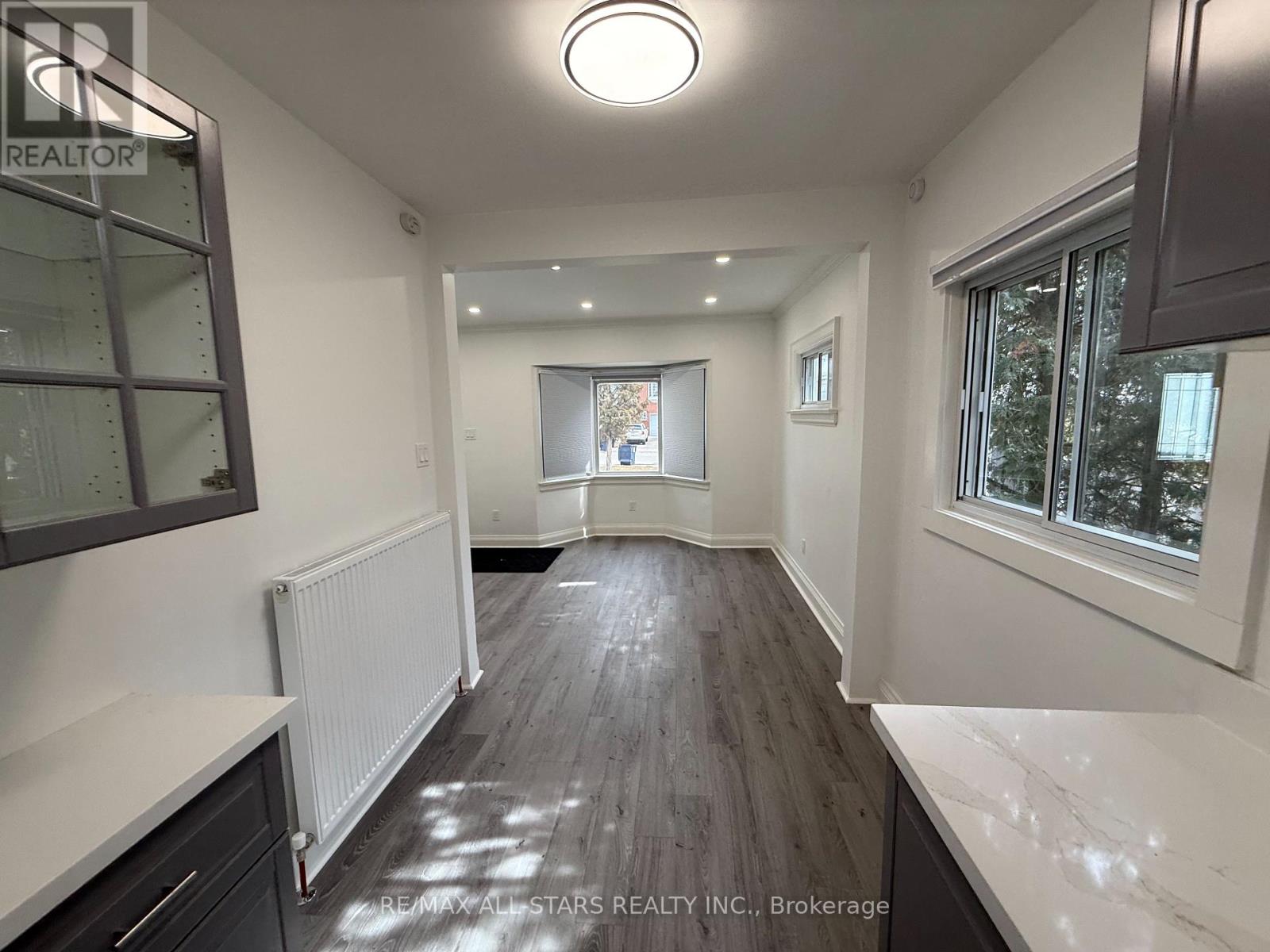 A spacious room with a white ceiling and wooden flooring.