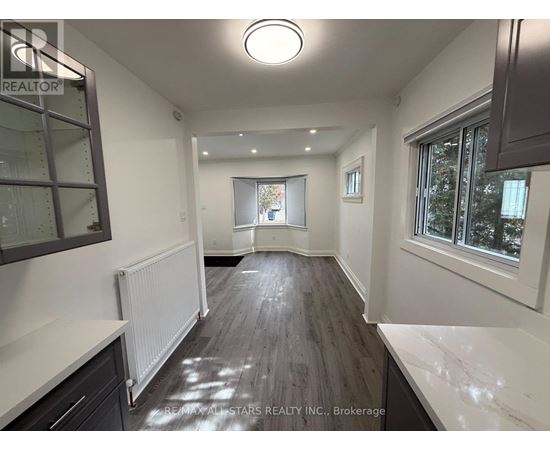 A spacious room with a white ceiling and wooden flooring.