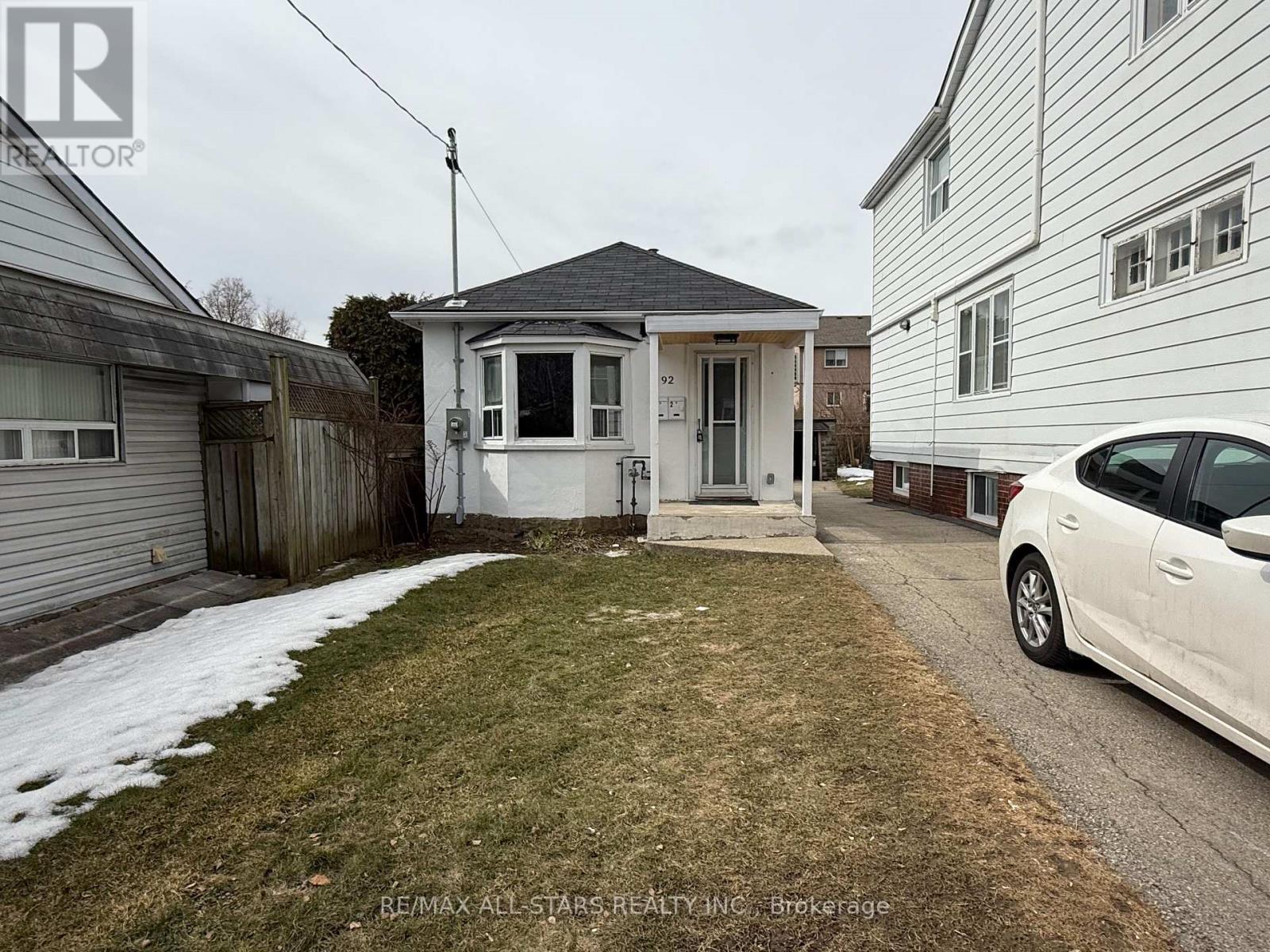 A white car is parked on a driveway in front of a house.