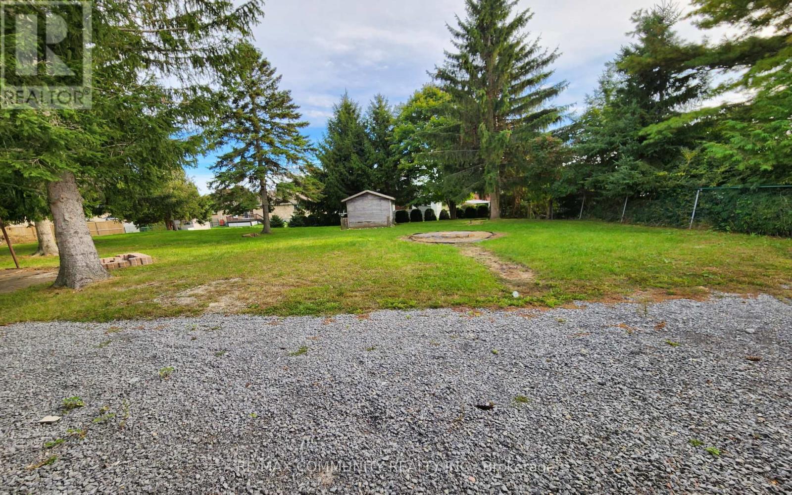 A gravel area leads to a grassy field with trees and a small building in the distance.
