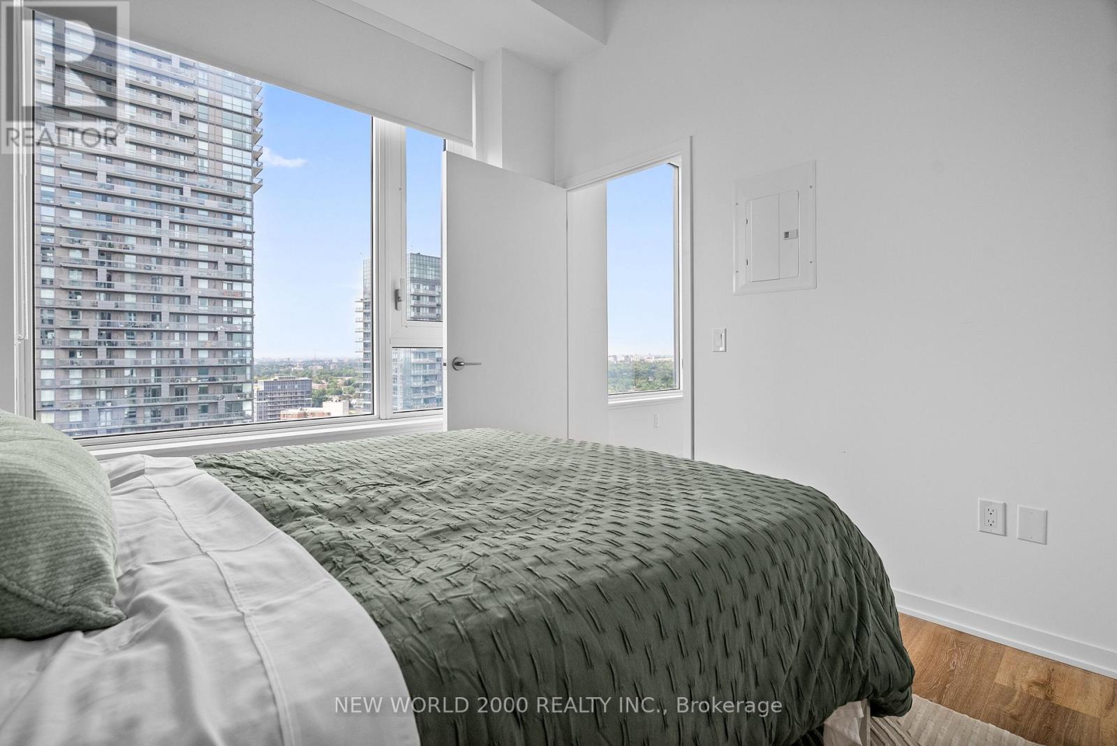 A bedroom with a large bed and a view of a building outside the window.