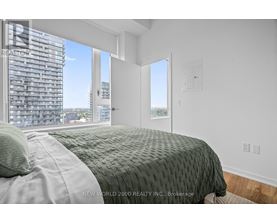 A bedroom with a large bed and a view of a building outside the window.