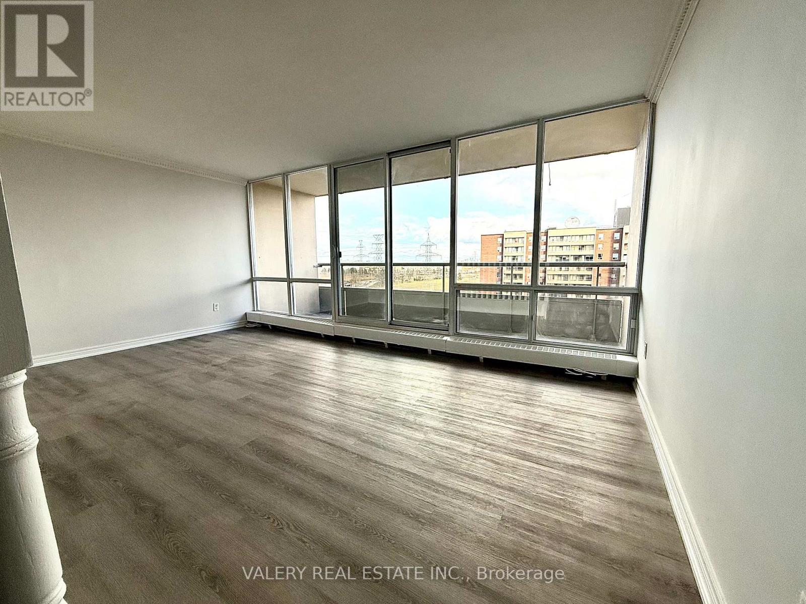 A room with wooden flooring and large windows overlooking a cityscape.