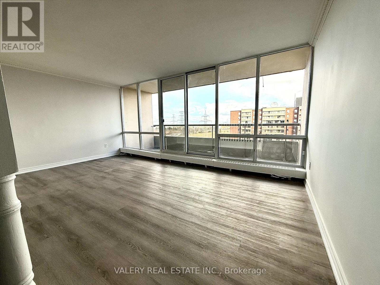 A room with wooden flooring and a large window with a view of buildings outside.