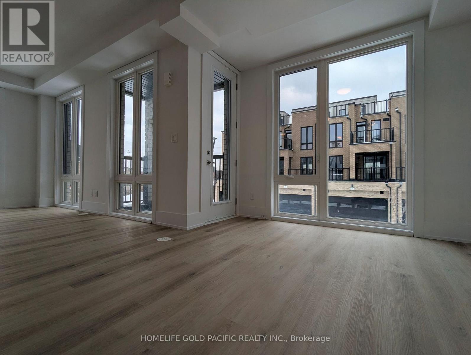 A spacious room with wooden flooring and large windows overlooking a cityscape.