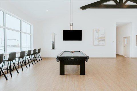 A pool table is in the middle of a room with a tv and chairs.