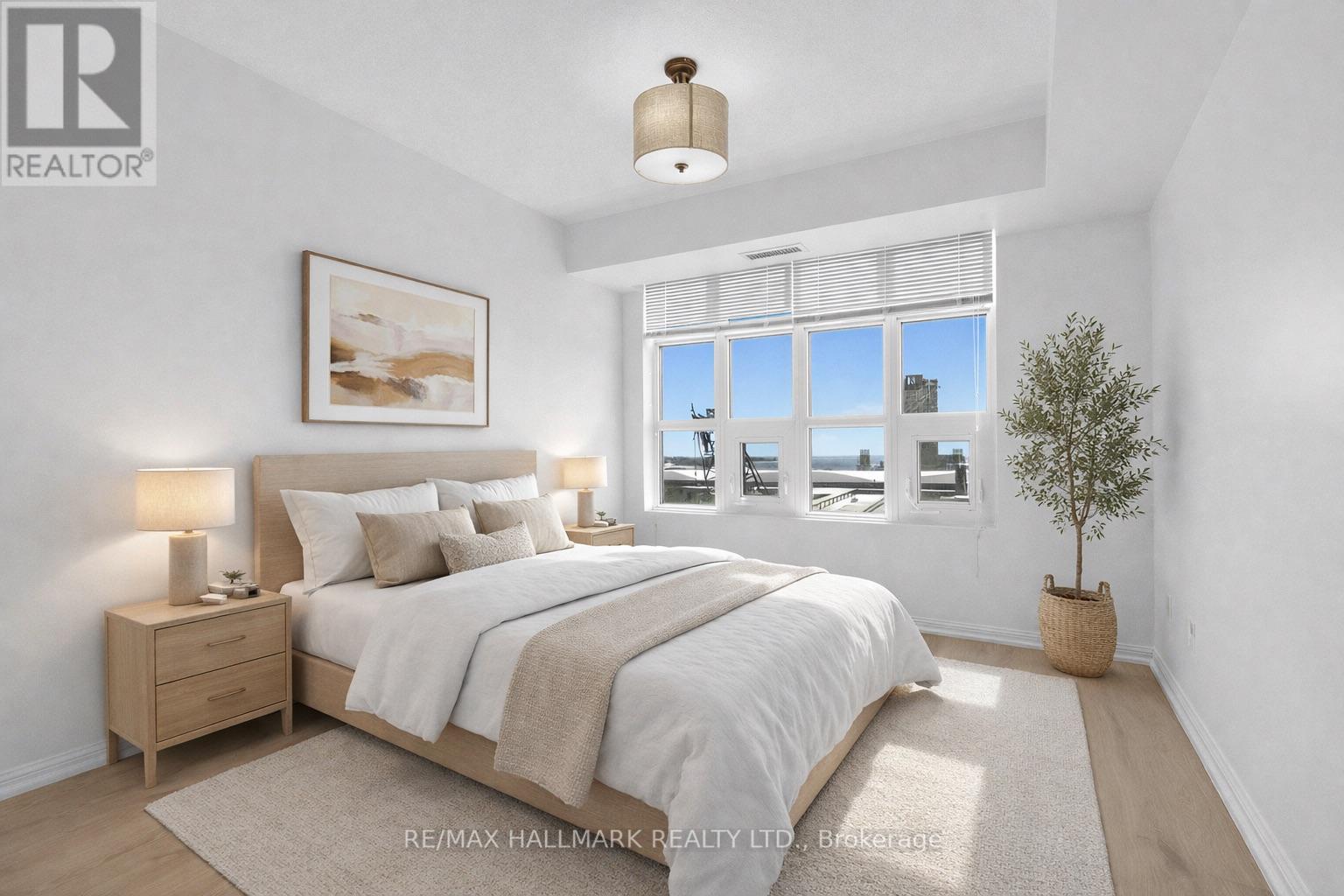 A bedroom with a large bed, a nightstand, a lamp, a framed picture on the wall, a window with blinds, and a potted plant.
