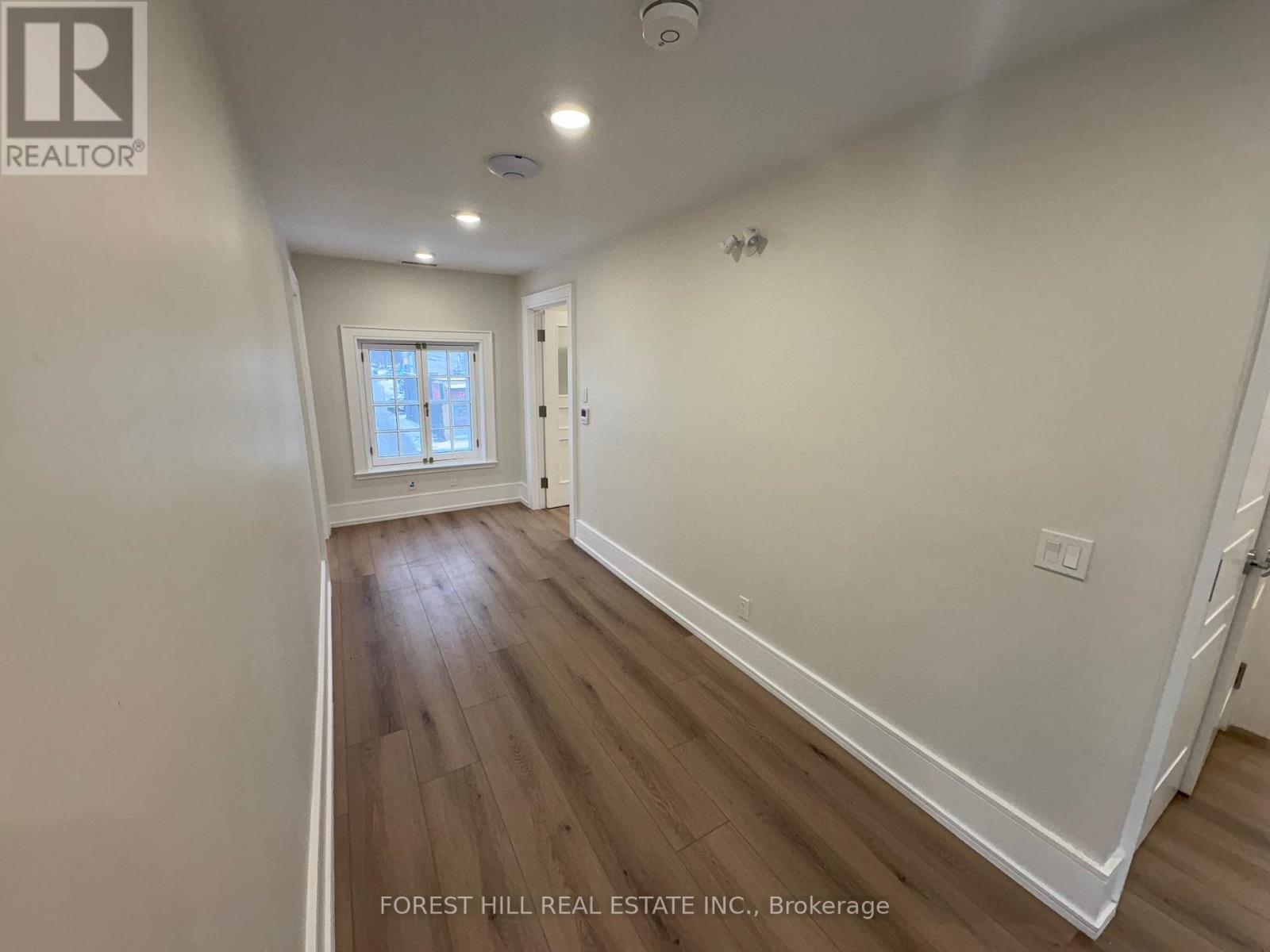 A room with wooden floors and white walls, with a window and a door visible.
