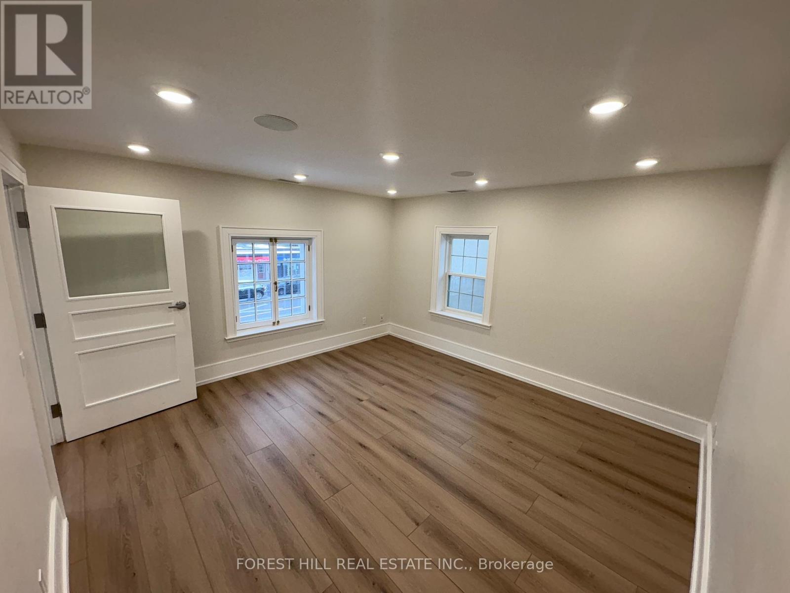 A room with wooden flooring and two windows.