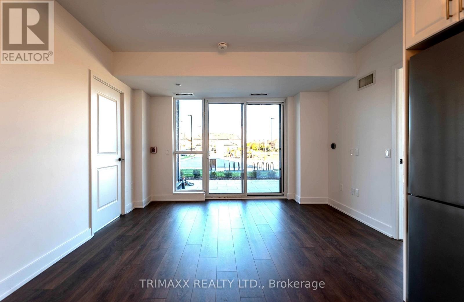 A spacious room with wooden floors and a view of the street through the windows.