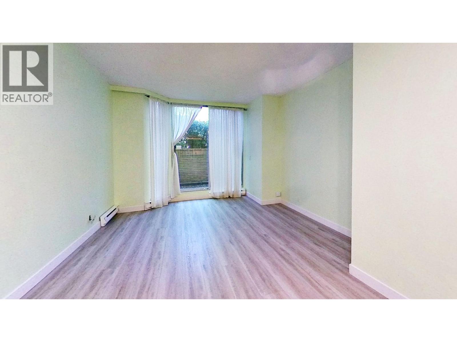 A room with wooden flooring and a window with curtains.