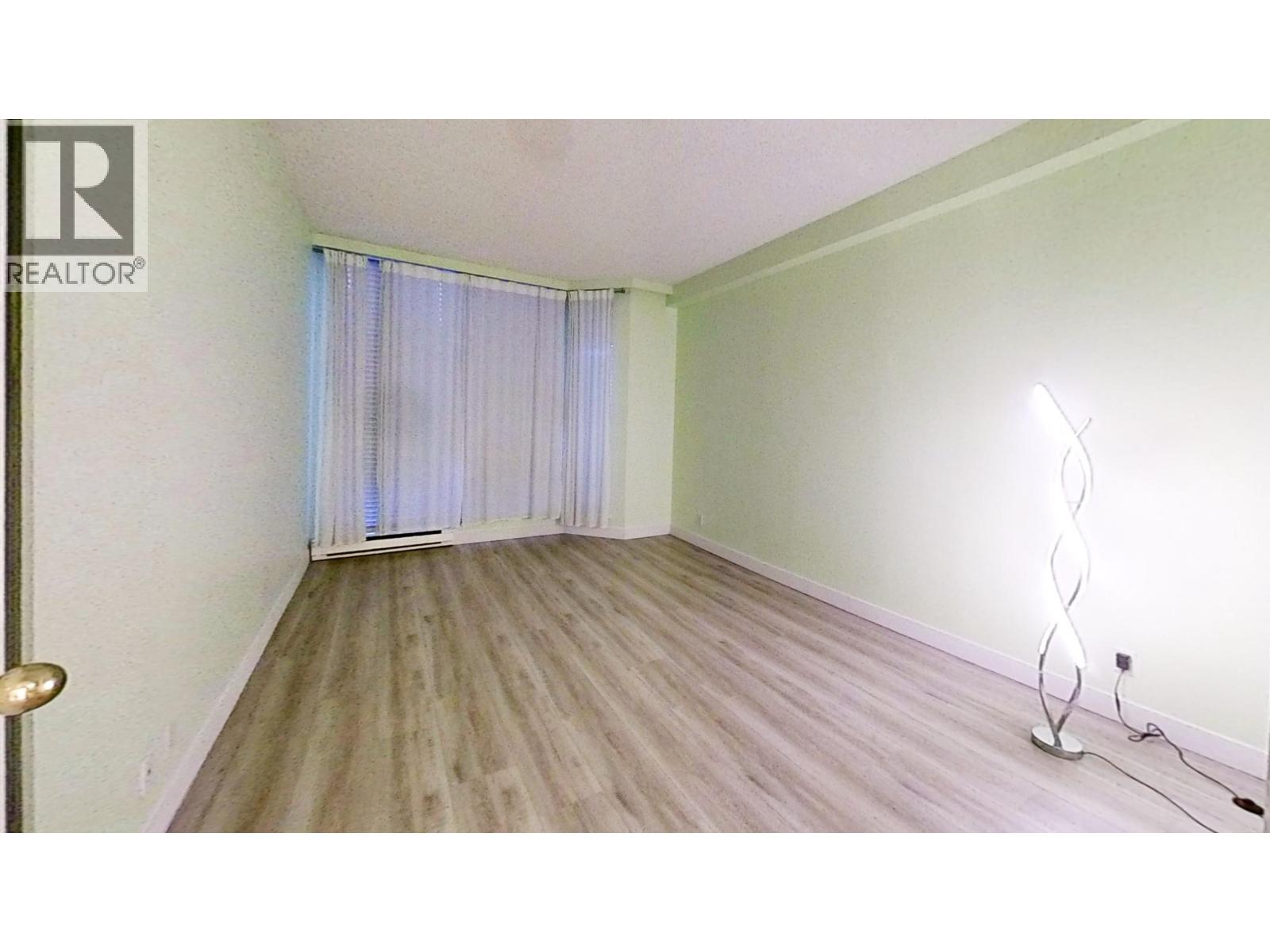 A room with a wooden floor and a window with curtains.