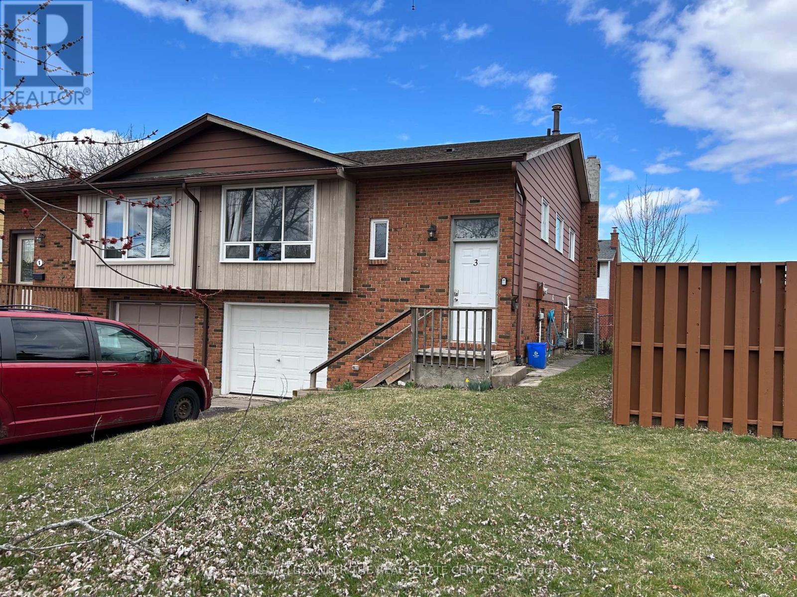 A red car is parked in front of a brick house with a white garage door.