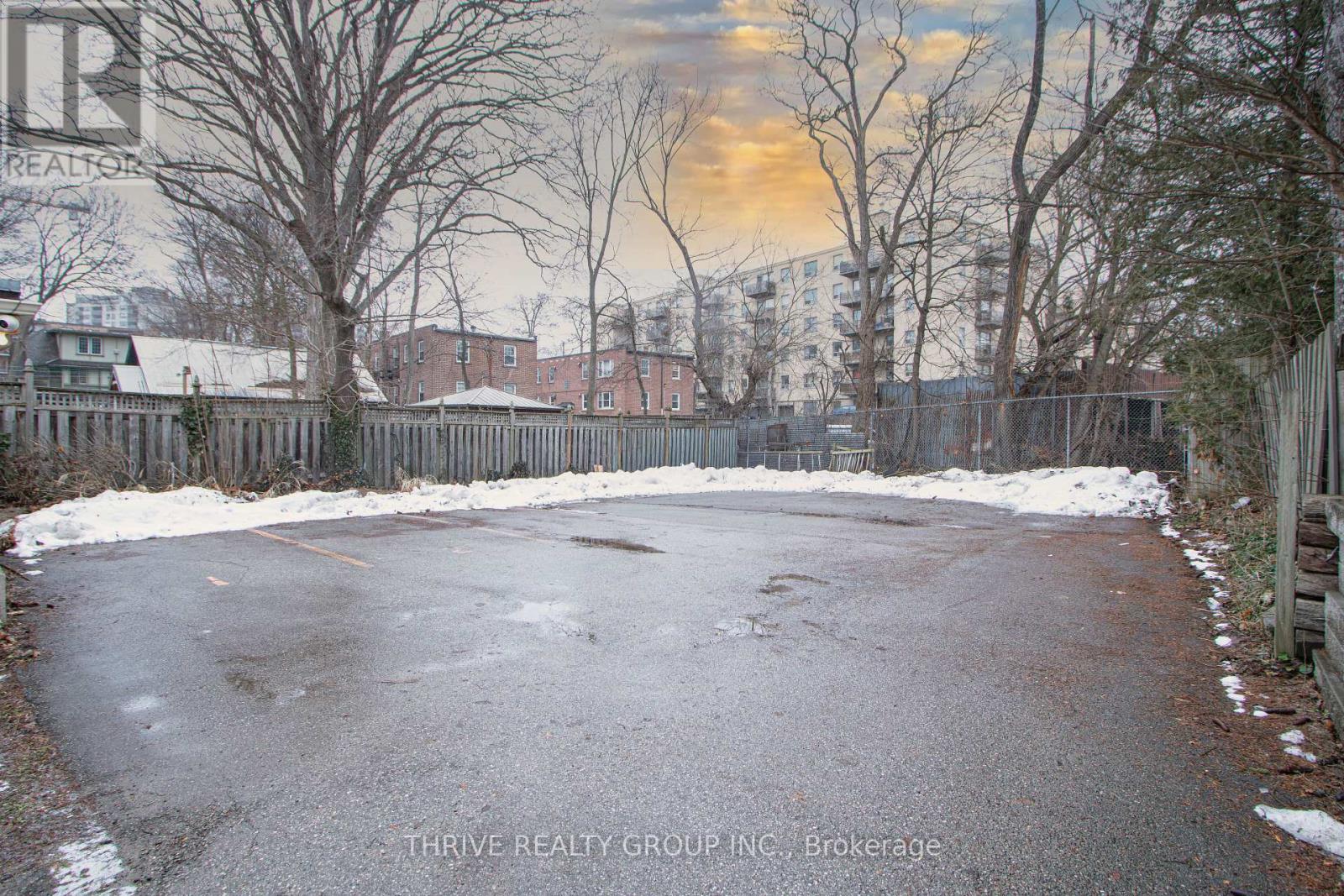 A snow-covered driveway leads to a house with a fence and bare trees.