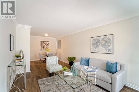 A living room with a grey couch, a glass coffee table, and a painting on the wall.