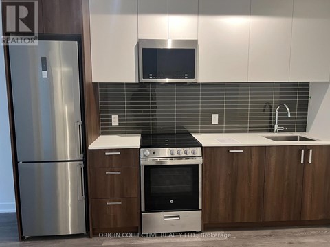A modern kitchen with a stainless steel refrigerator, a microwave above the stove, and wooden cabinets.