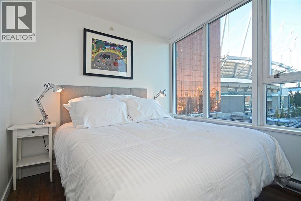 A bedroom with a large bed, a nightstand with a lamp, and a framed picture on the wall.