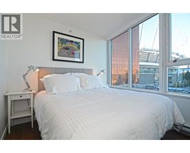 A bedroom with a large bed, a nightstand with a lamp, and a framed picture on the wall.