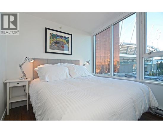 A bedroom with a large bed, a nightstand with a lamp, and a framed picture on the wall.