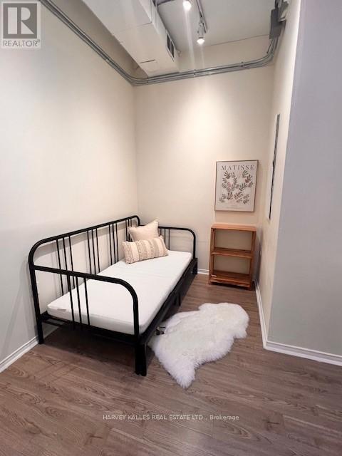 A bedroom with a black metal frame bed, a small wooden shelf, and a white fluffy rug.