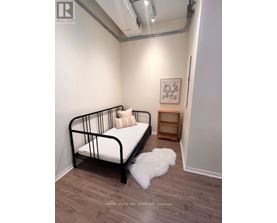 A bedroom with a black metal frame bed, a small wooden shelf, and a white fluffy rug.