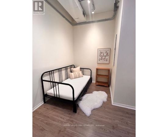 A bedroom with a black metal frame bed, a small wooden shelf, and a white fluffy rug.