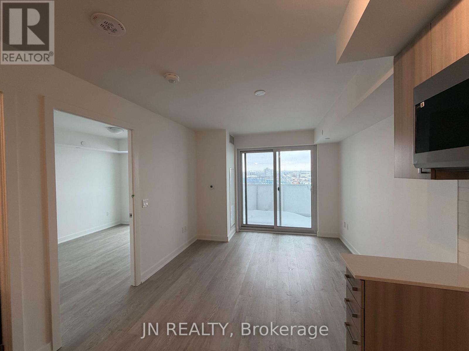 A spacious room with wooden flooring and a sliding glass door leading to a balcony.
