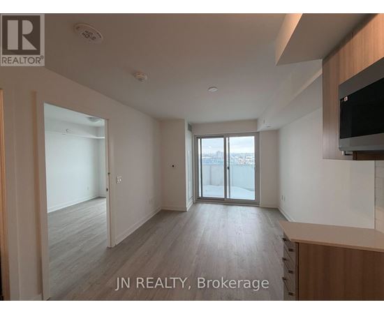 A spacious room with wooden flooring and a sliding glass door leading to a balcony.