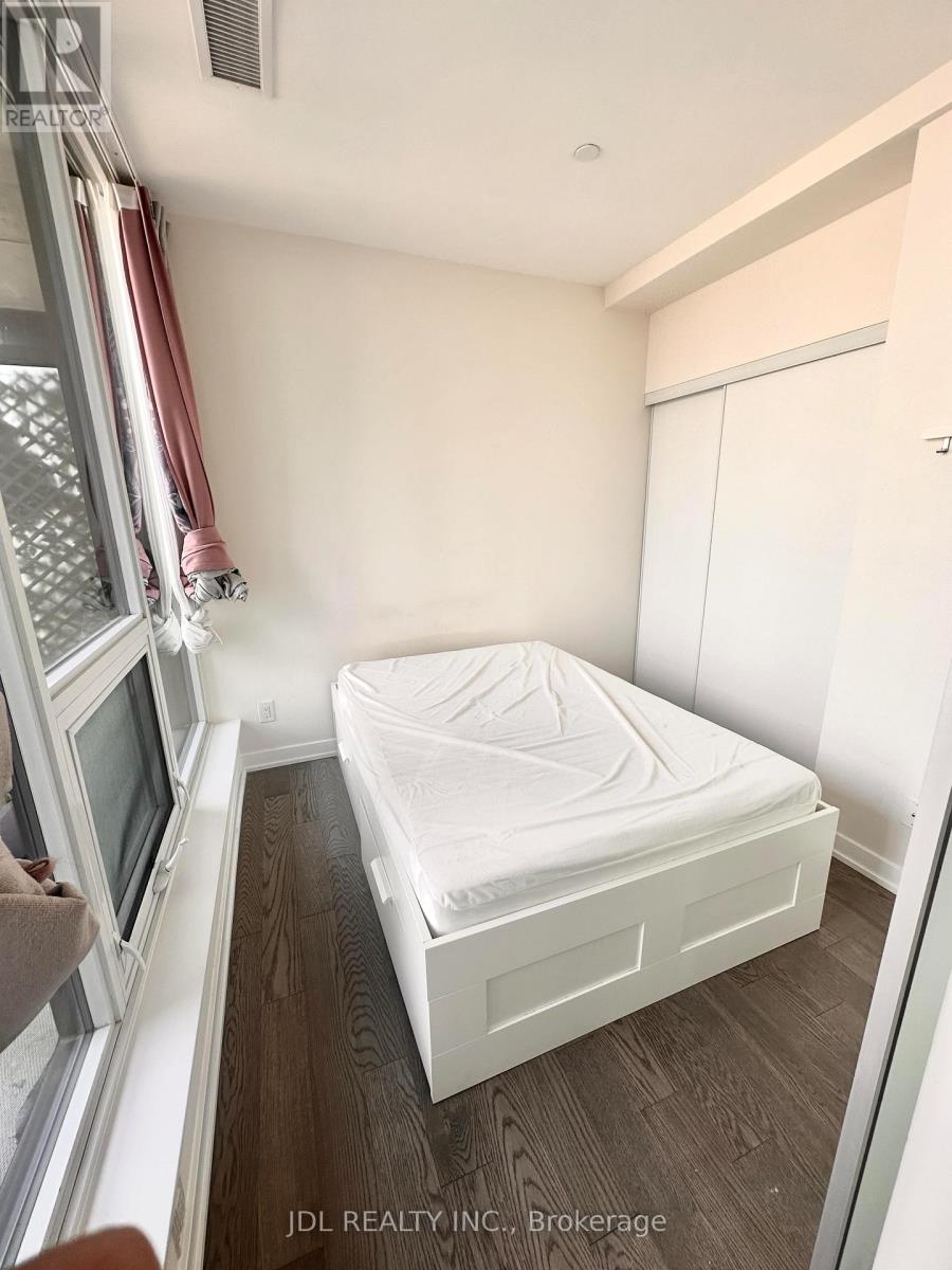 A small bedroom with a bed, a window with a red curtain, and a wooden floor.