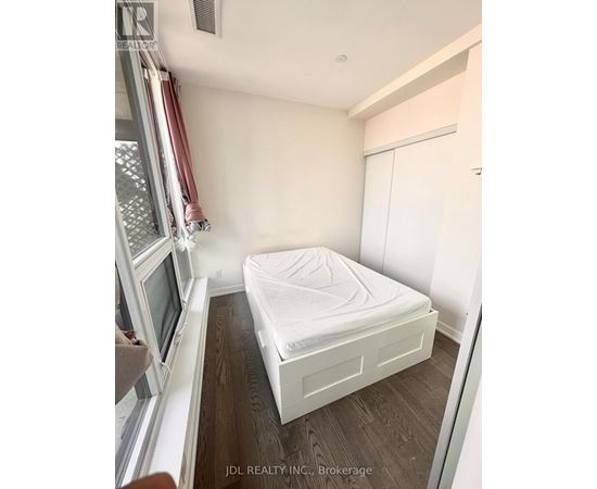 A small bedroom with a bed, a window with a red curtain, and a wooden floor.