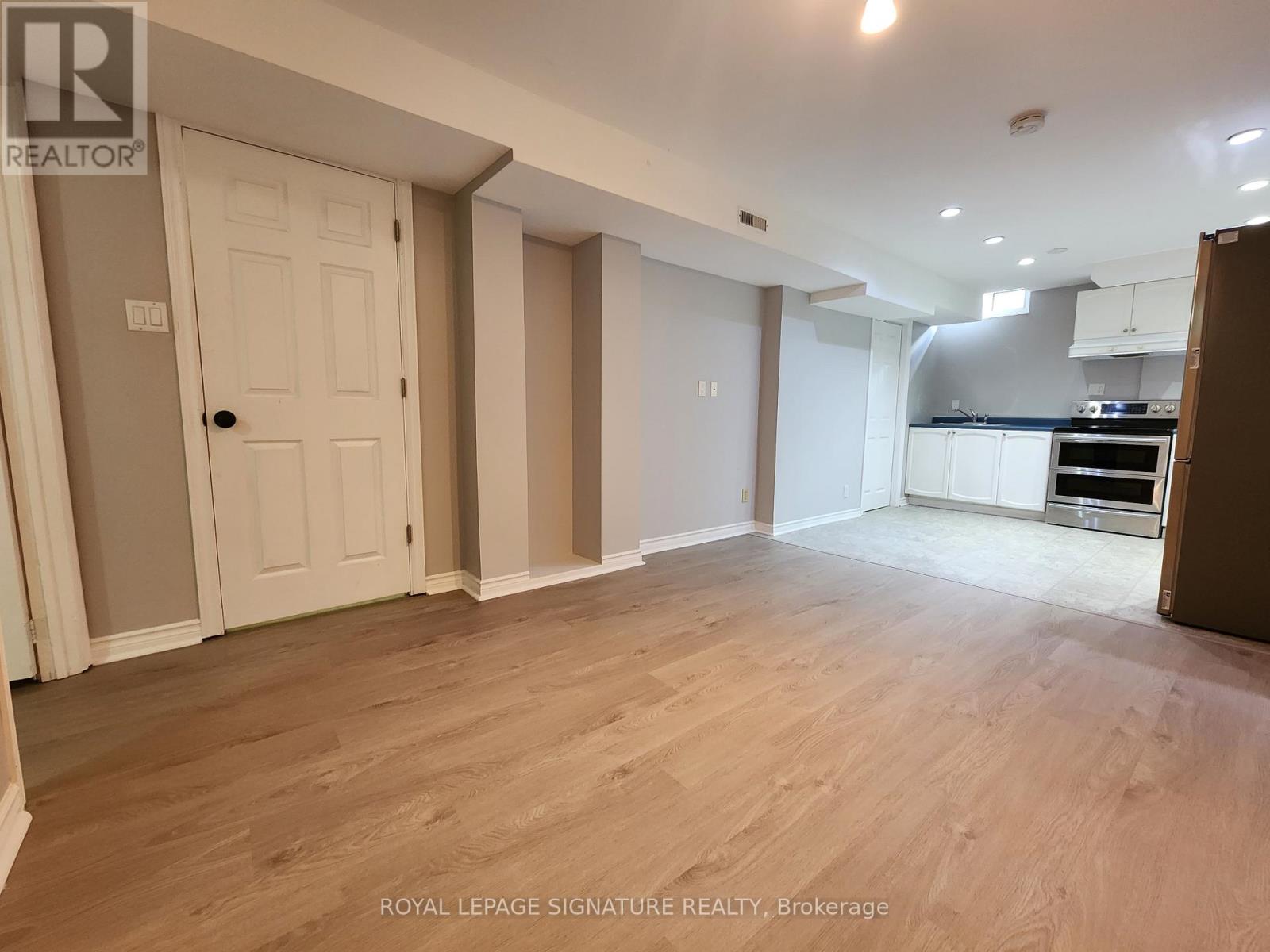 A spacious room with wooden flooring and a kitchen area in the background.