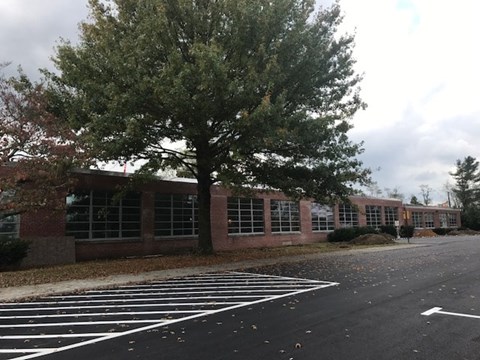 A parking lot in front of a brick building with a tree.