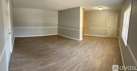 A spacious room with wooden flooring and white walls.