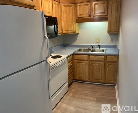 A kitchen with a white refrigerator, wooden cabinets, and a stove top oven.
