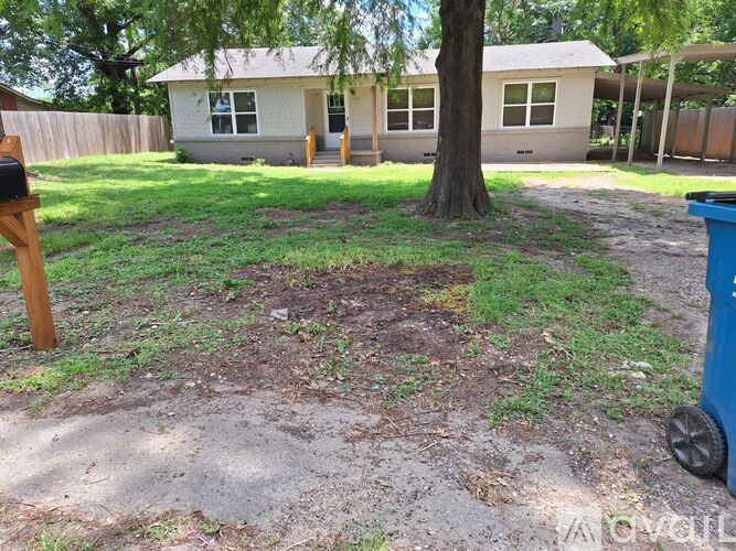 A backyard with a tree, a mailbox, and a trash can.
