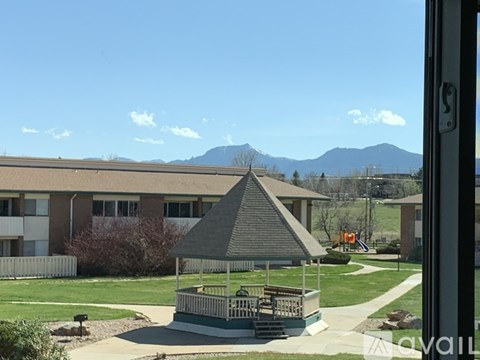 A gazebo sits in the middle of a grassy area in front of a building.