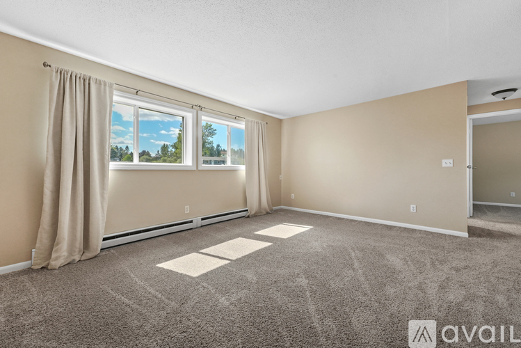 A room with beige walls and carpeting, a window with a view of trees, and a door on the right.