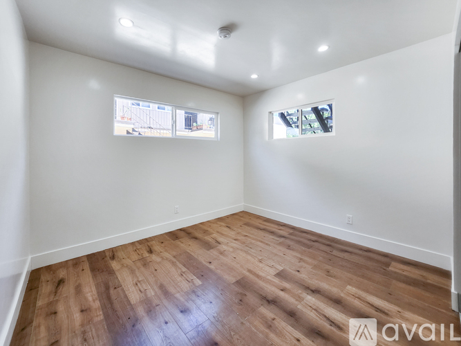A room with wooden flooring and two windows.