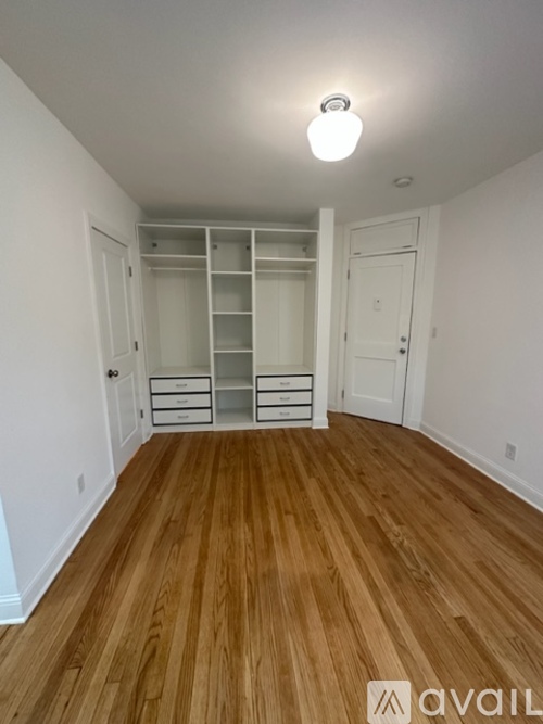 A room with wooden floors and white walls, featuring a built-in shelving unit and a single light fixture.