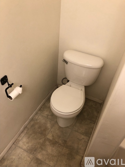 A white toilet in a small bathroom with a roll of toilet paper on the wall.