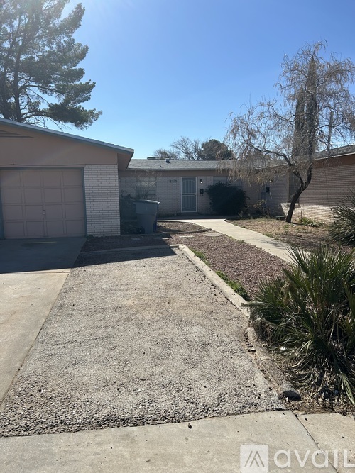 A gravel driveway leads to a garage with a tree and a house in the background.