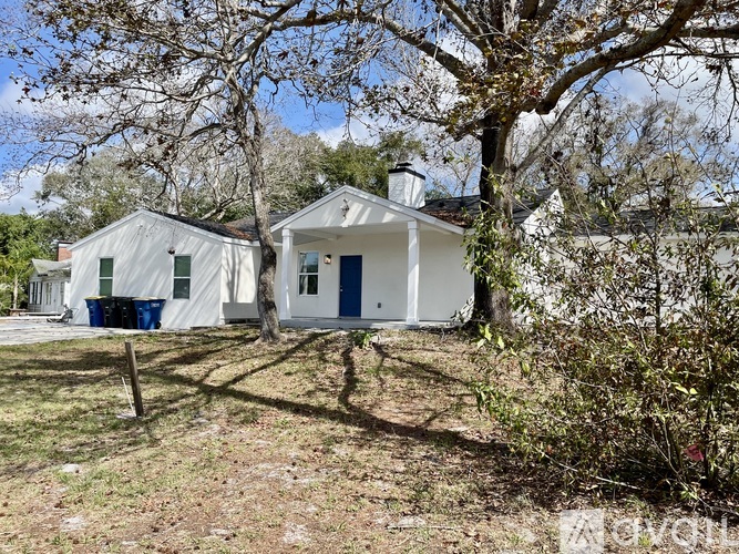 A white house with a blue door is surrounded by trees.