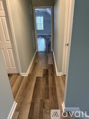 A hallway with wood flooring and white walls leading to a door.