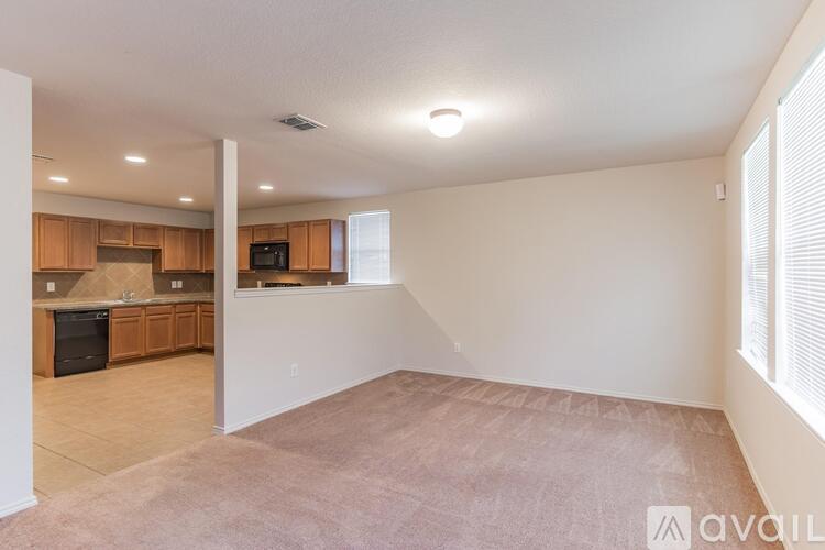 A spacious living room with a kitchen in the background and a carpet on the floor.