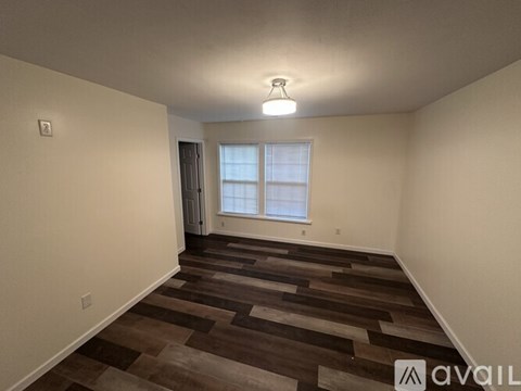 A room with wooden flooring and a window with white curtains.