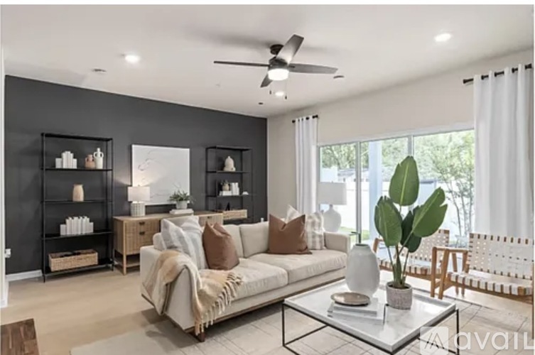 A living room with a couch, a plant, and a fan.