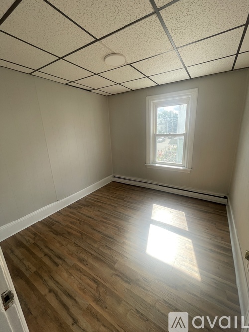 A room with wooden flooring and a window letting in sunlight.