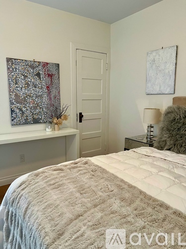 A bedroom with a bed, a nightstand with a lamp, and two paintings on the wall.